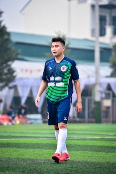 Focused soccer player on the field in Hanoi, Vietnam, wearing blue and green uniform.