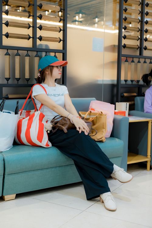 Free Woman sitting indoors surrounded by shopping bags, wearing casual attire and a cap. Stock Photo