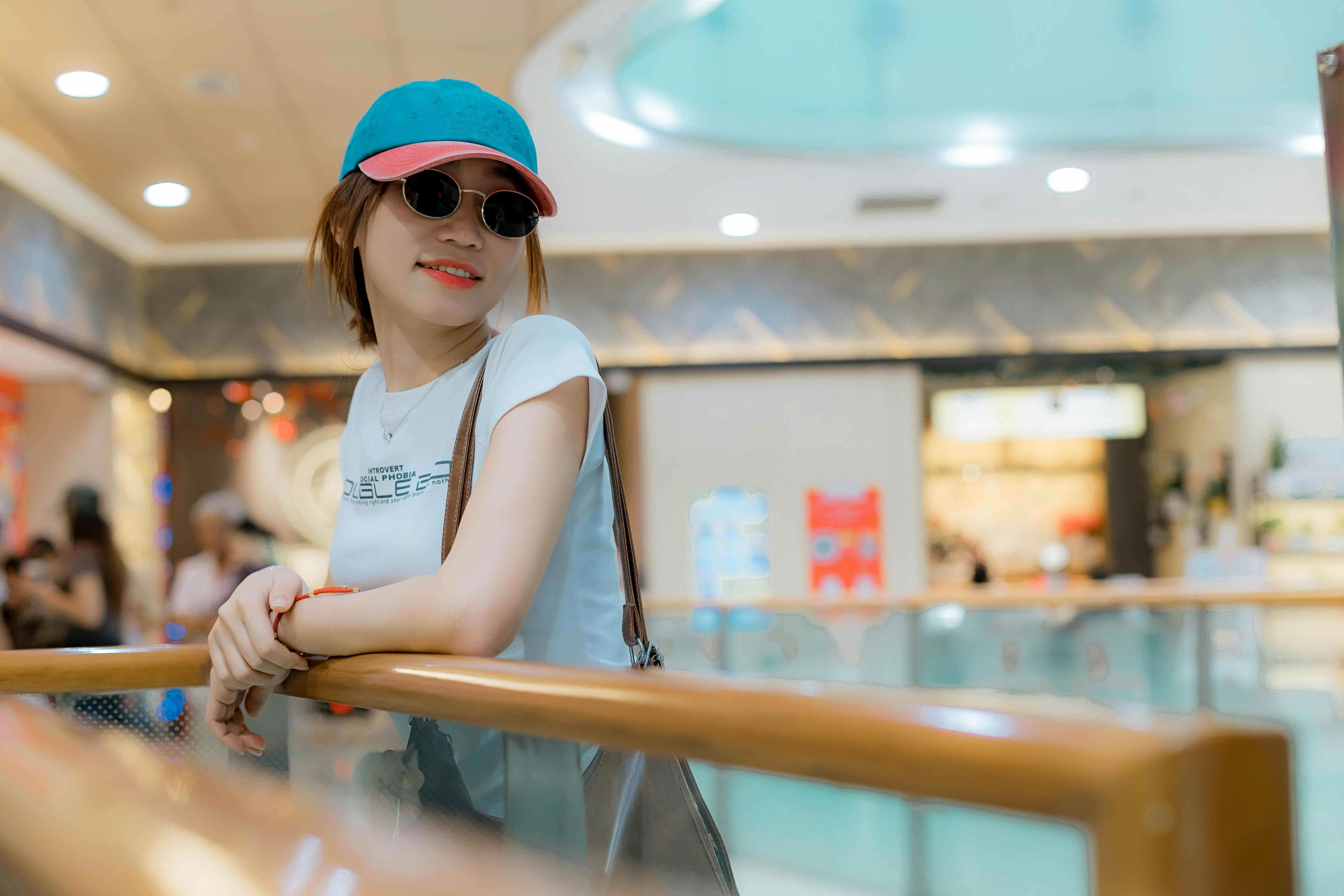 Miễn phí Người phụ nữ sành điệu với mũ và kính râm đang tựa vào lan can trong nhà. Ảnh lưu trữ