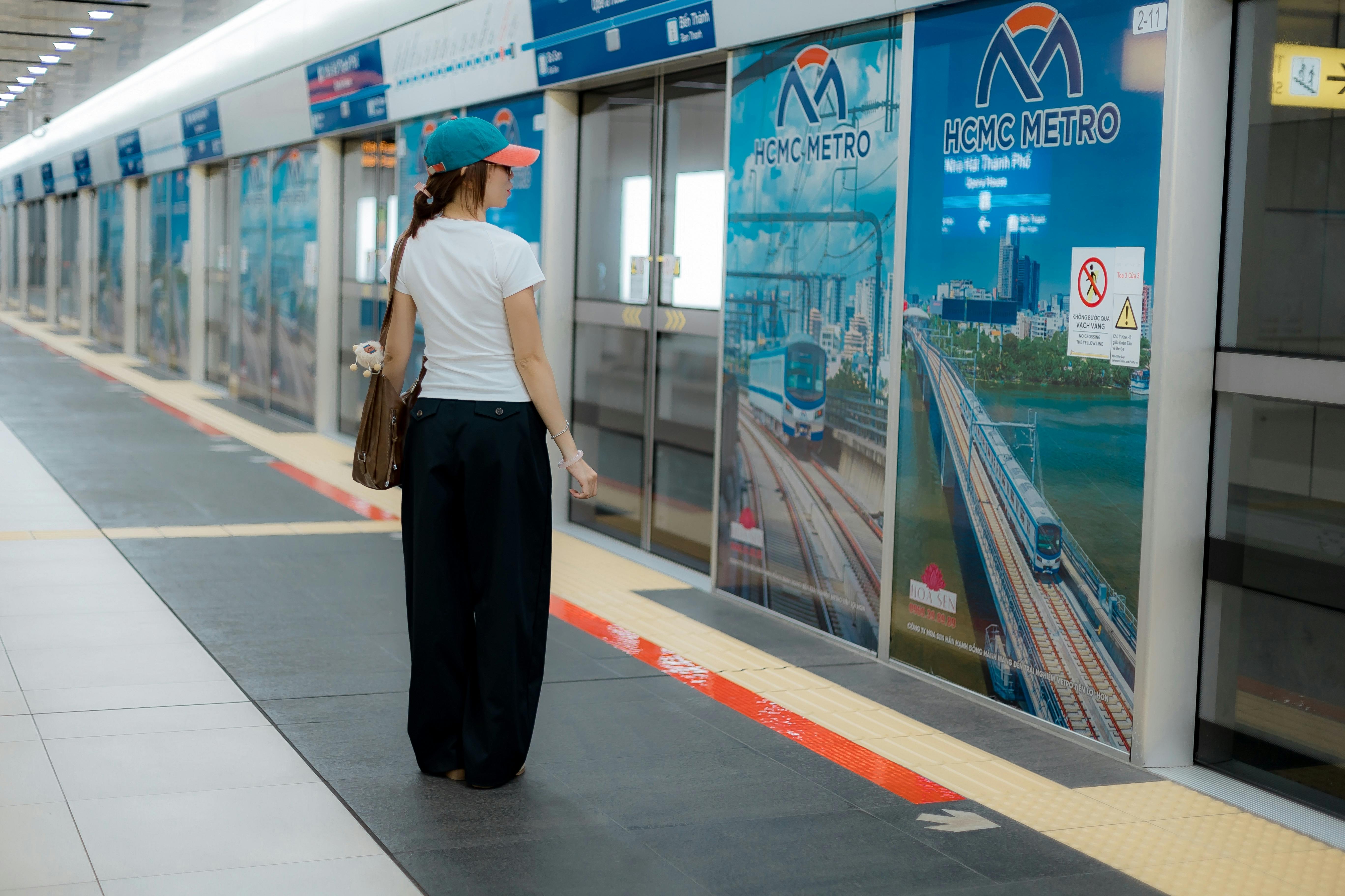 A woman in casual attire waits at HCMC Metro station platform, capturing urban transport scene.