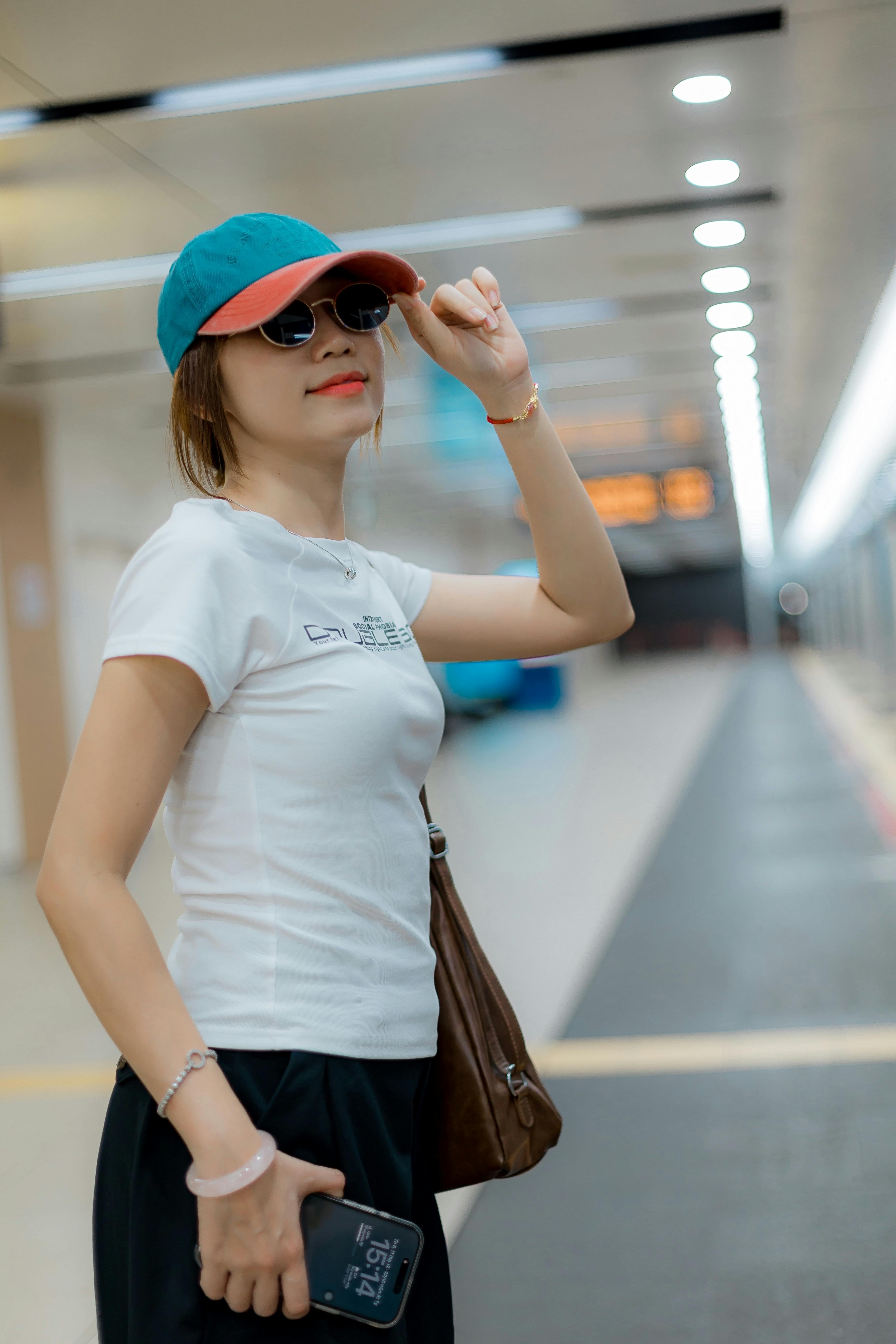 Fashionable woman in sunglasses and cap in a modern subway station, exuding confidence and style.