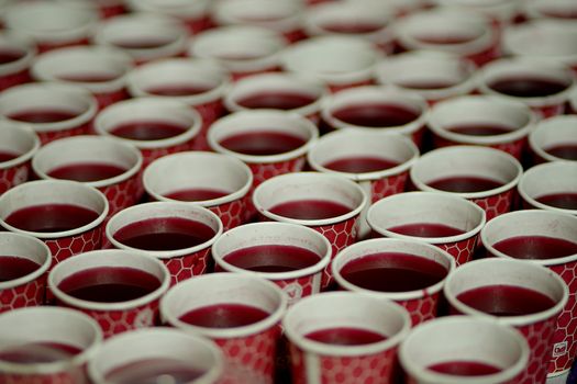 Close-up of multiple red juices in patterned paper cups, symmetrically arranged.