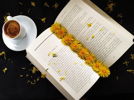 Open book with yellow flowers and coffee on a black background, creating a cozy reading atmosphere.