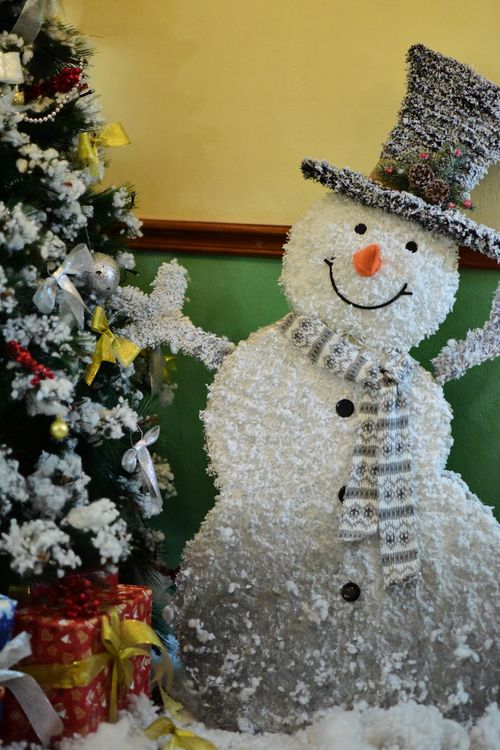 Free Smiling snowman decoration with a Christmas tree and gifts, indoors. Stock Photo