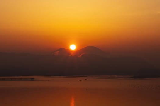 A breathtaking sunset with the sun setting over silhouetted mountains, casting a warm glow.