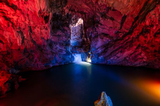Colorful cave interior with illuminated walls and a waterfall cascading into a serene pool.