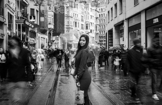 Black and white photo of a woman on a rainy Istiklal Street, Istanbul, with umbrellas.