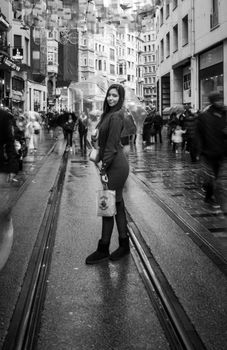 A woman with an umbrella stands on rainy Istiklal Street in Istanbul, creating a lively urban scene.