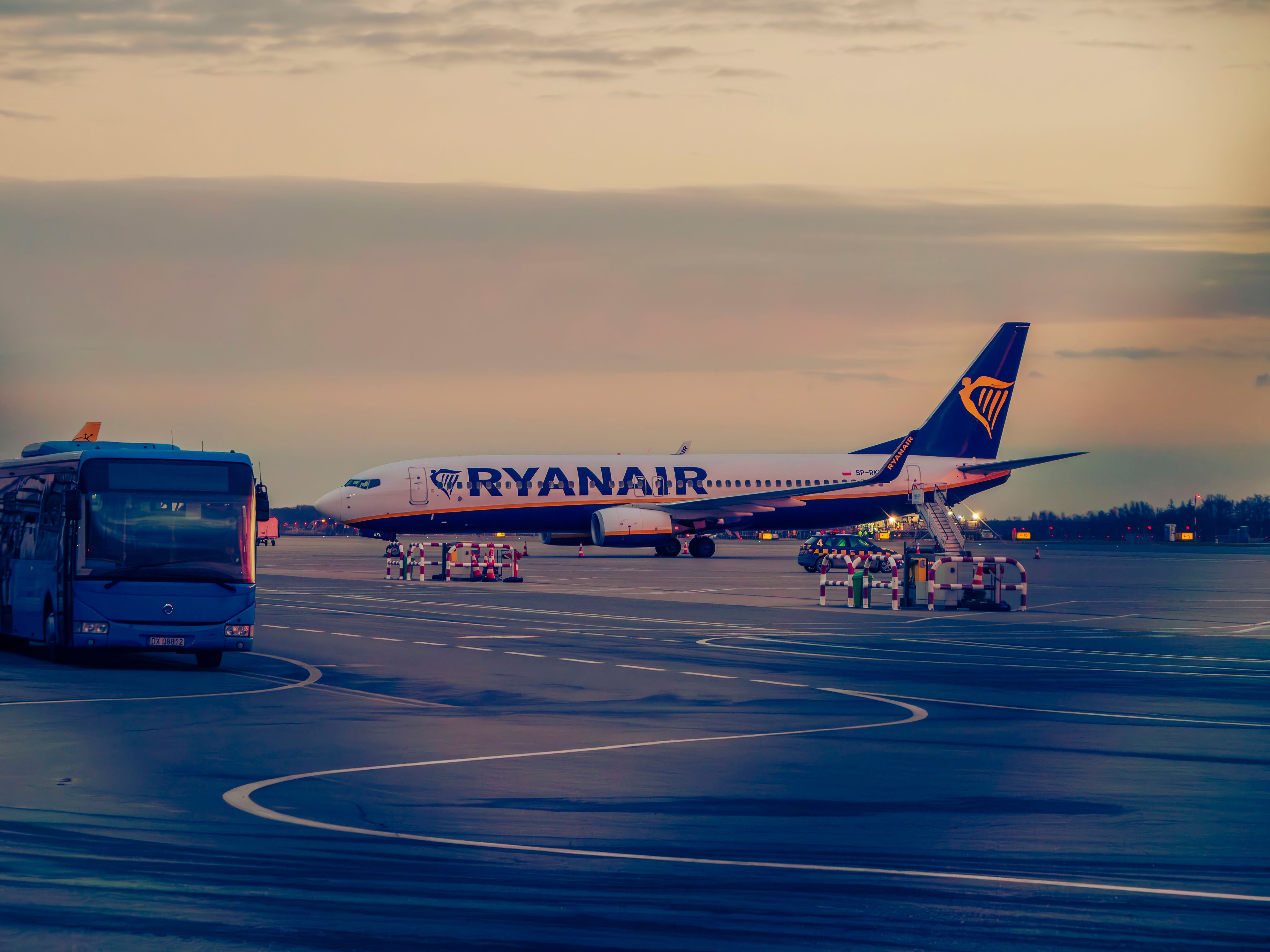 Ryanair aircraft with a shuttle bus on the tarmac at sunset in Wrocław, Poland.