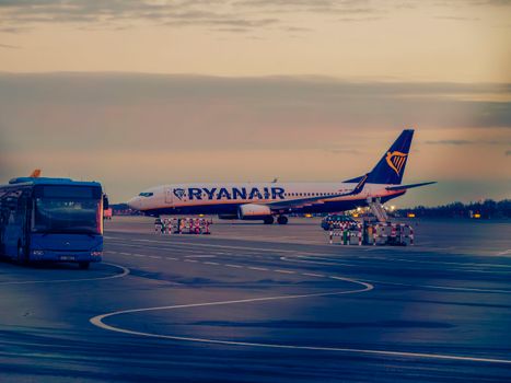 Ryanair aircraft with a shuttle bus on the tarmac at sunset in Wrocław, Poland.