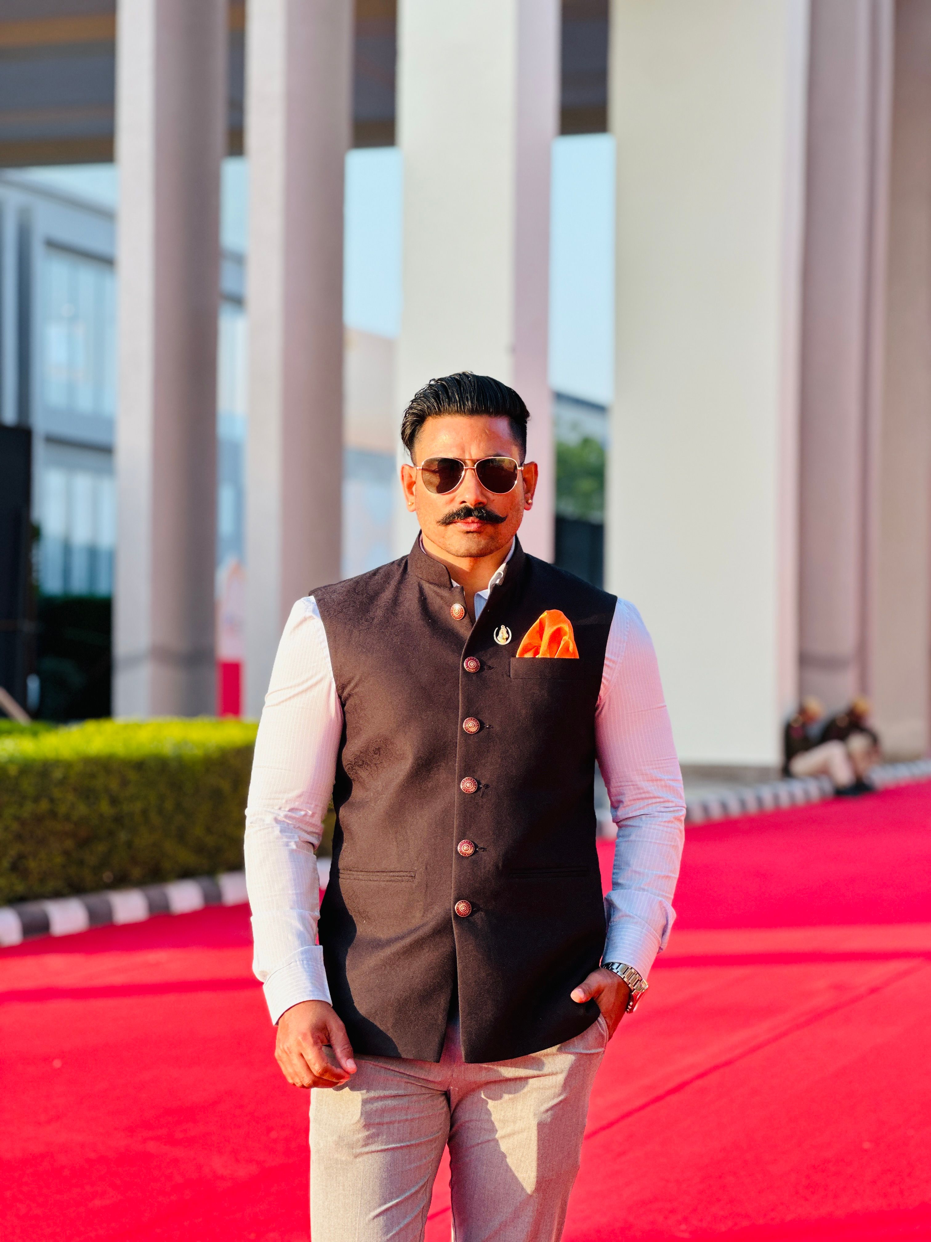 Man in stylish attire poses confidently on a vibrant red carpet outdoors.