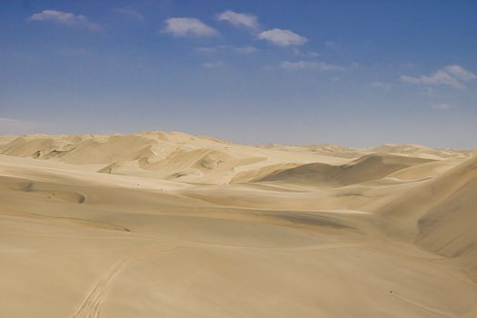 Serene aerial view of rolling sand dunes under a clear blue sky in the Namibian desert.