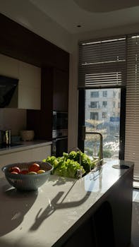 A modern kitchen interior with sunlight illuminating fresh vegetables and stylish decor.