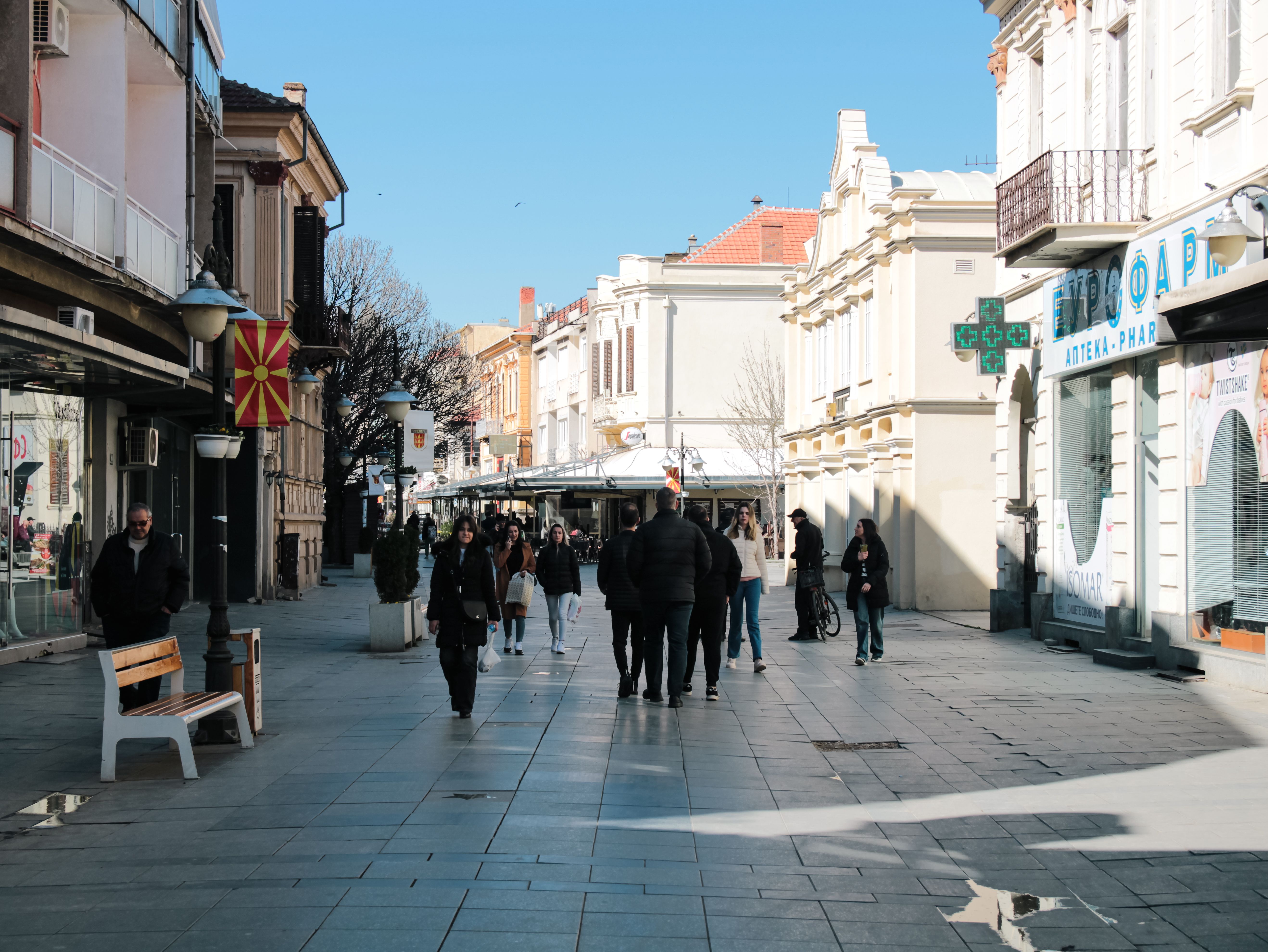 A lively pedestrian street scene with people walking under clear skies on a sunny day.