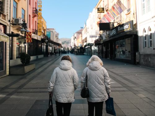 Free Two women in winter coats walking down a colorful city street on a clear day. Stock Photo
