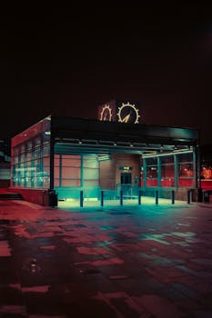A modern metro station glowing with neon lights in a moody cityscape at night.