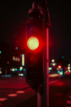 Moody urban night scene featuring a glowing red traffic light and blurred city lights.