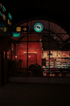 A cozy café scene with neon lights seen through a window at night.