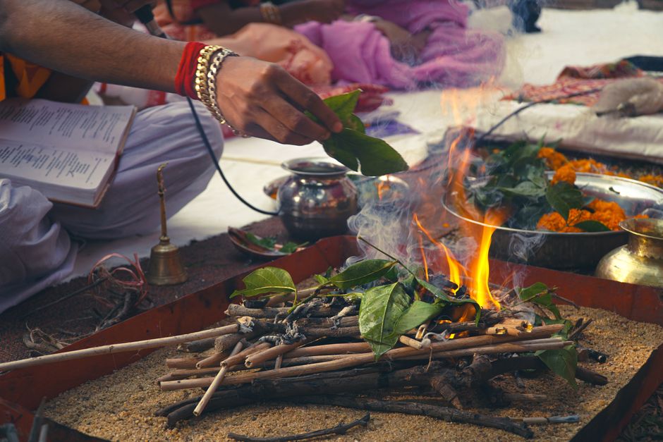 A close-up of a Hindu ceremony with a ritual fire, leaves, and offerings.