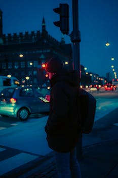 A person on a smartphone at a neon-lit street in Copenhagen at night.