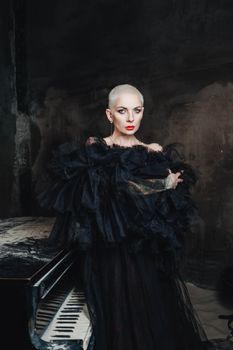 Dramatic portrait of a woman in black tulle, standing by a piano.