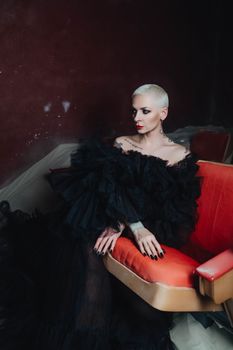 Striking portrait of a woman in a black gown sitting in a vintage red chair.