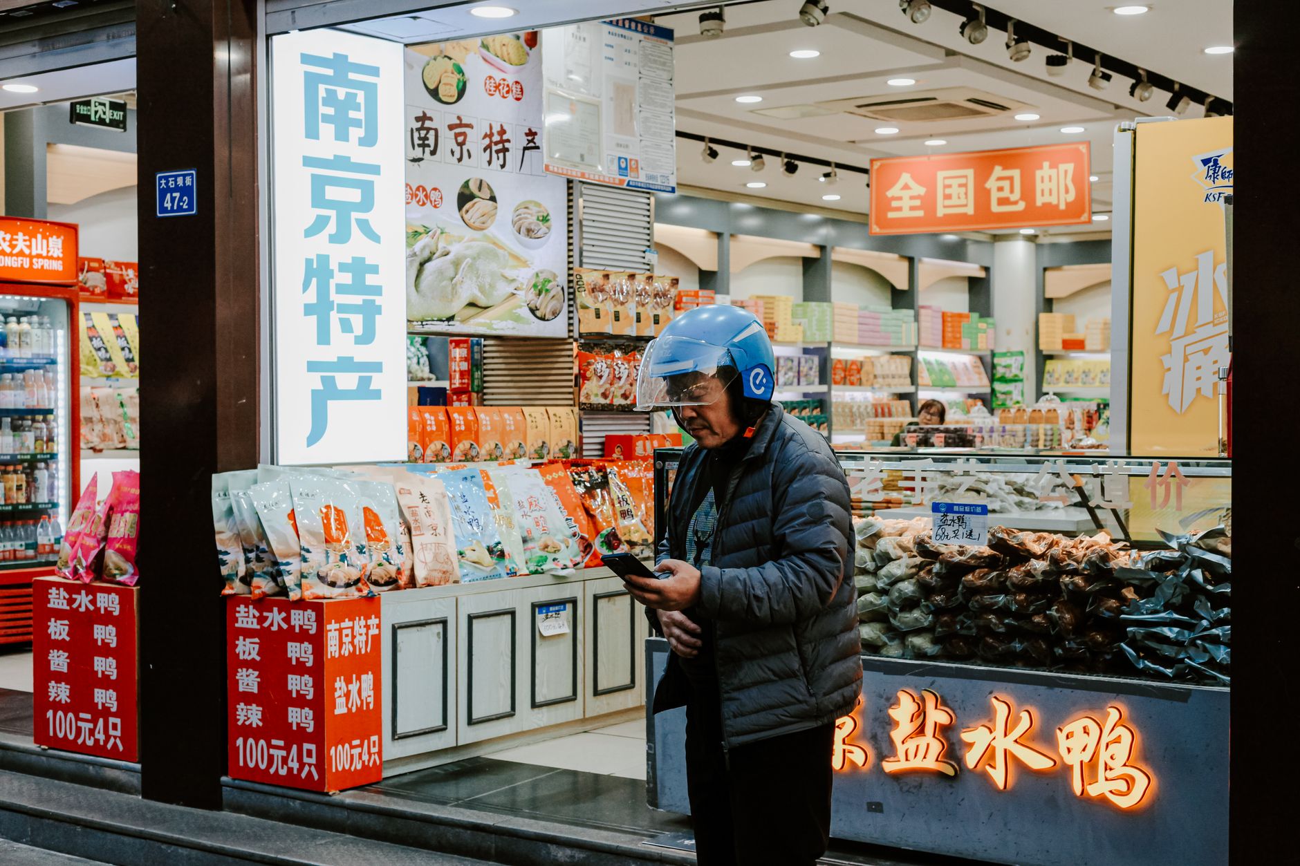 Explore the bustling urban life of Nanjing with this vibrant street market scene featuring local shops and a passerby.