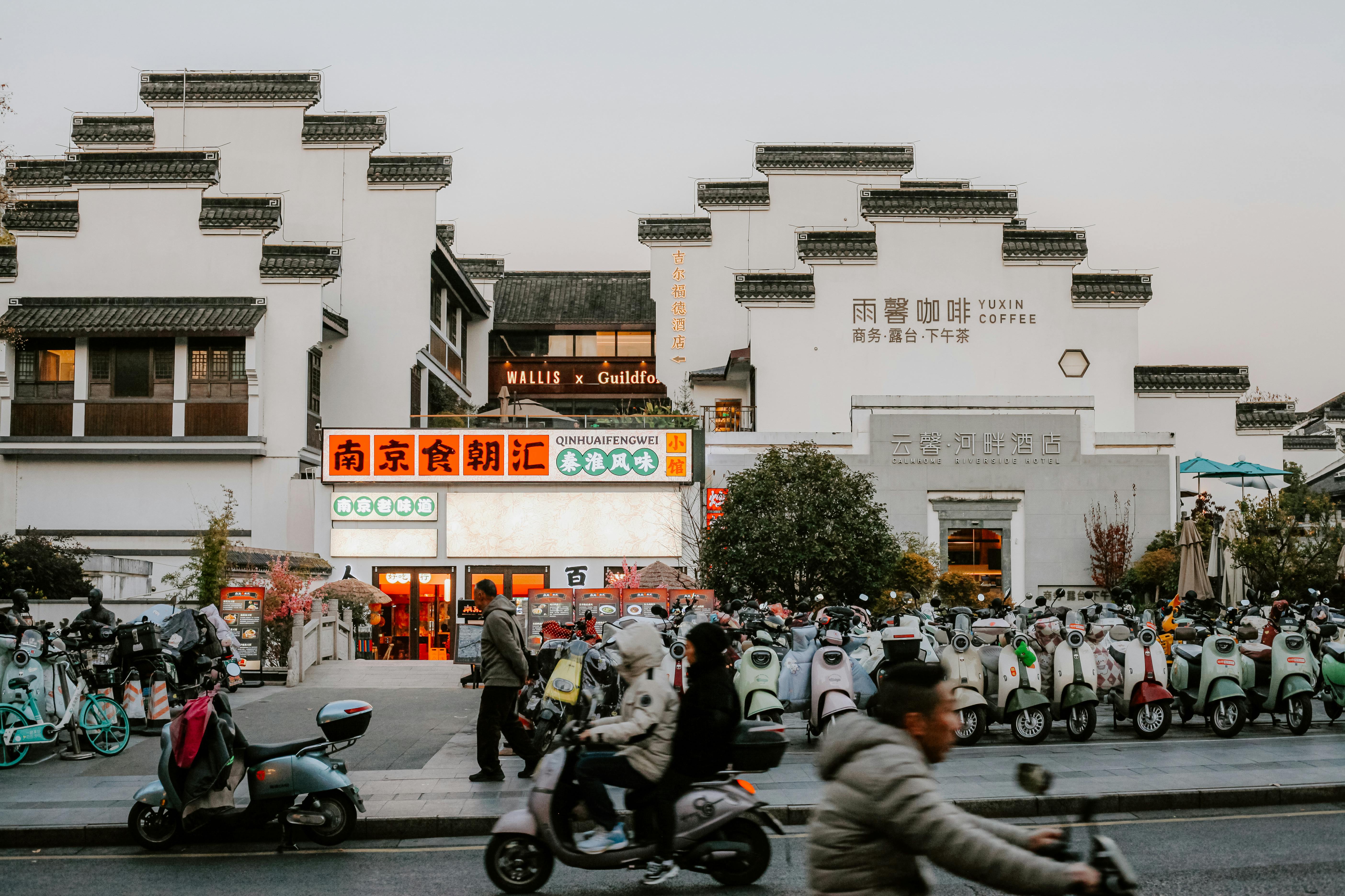 A lively street in Nanjing featuring traditional architecture, scooters, and urban life.