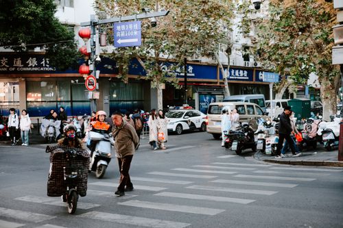 Free Street life in Nanjing, China with people, scooters, and autumn foliage on a busy corner. Stock Photo