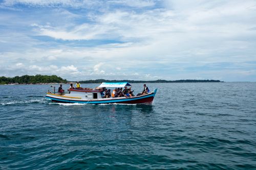 Free A group enjoys a boat ride across clear waters with a scenic tropical backdrop. Stock Photo