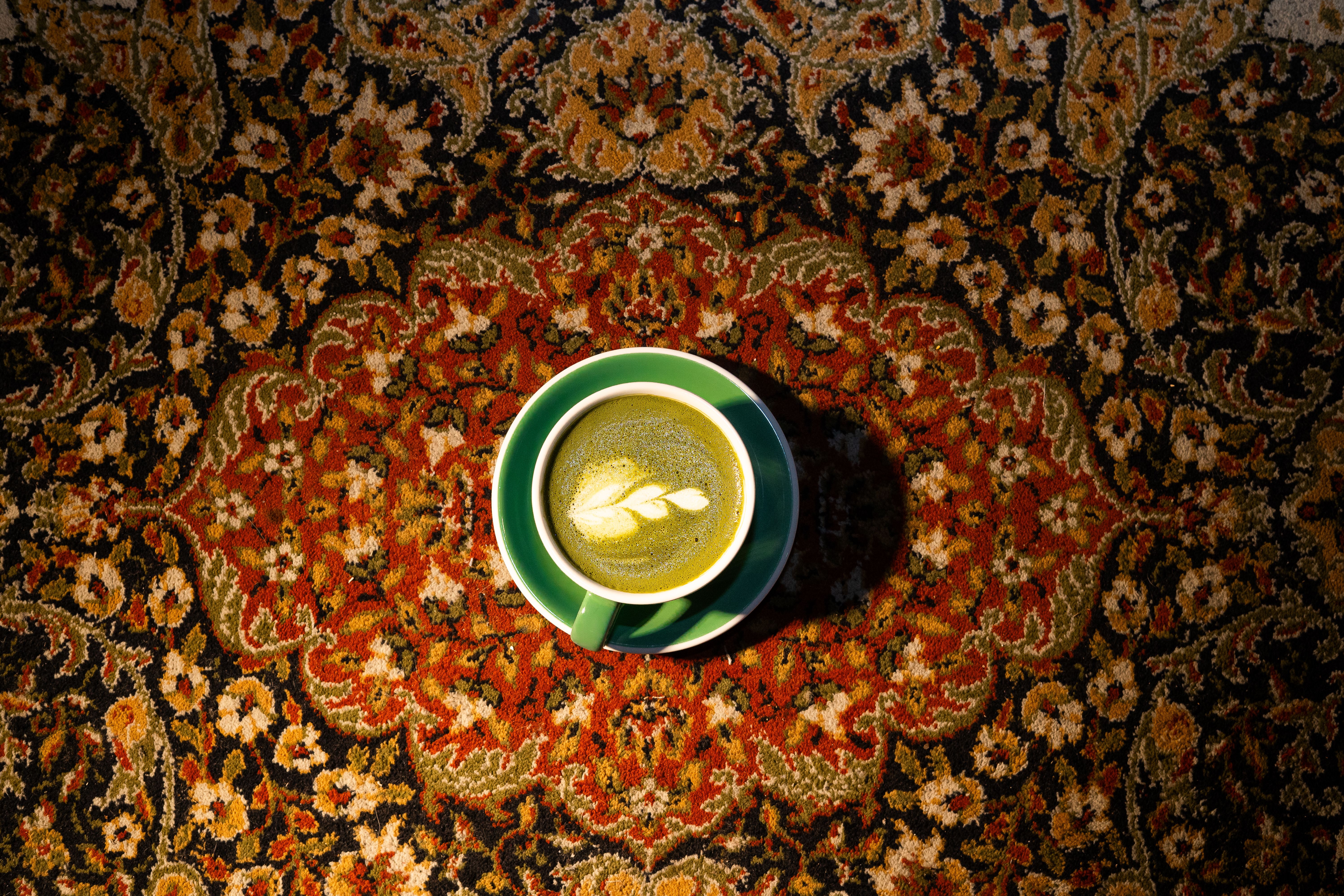 A top view of a matcha latte with latte art, placed on an ornate Persian rug.