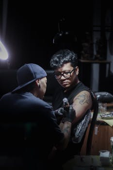 A tattoo artist skillfully inking a client in a dimly lit West Java studio setting.