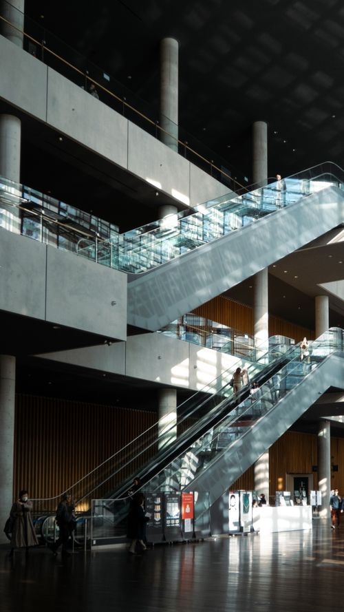 Free Contemporary indoor architecture featuring glass escalators and concrete columns in natural light. Stock Photo
