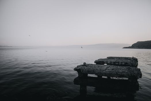 A tranquil seascape with an old concrete pier extending into calm waters at dusk.