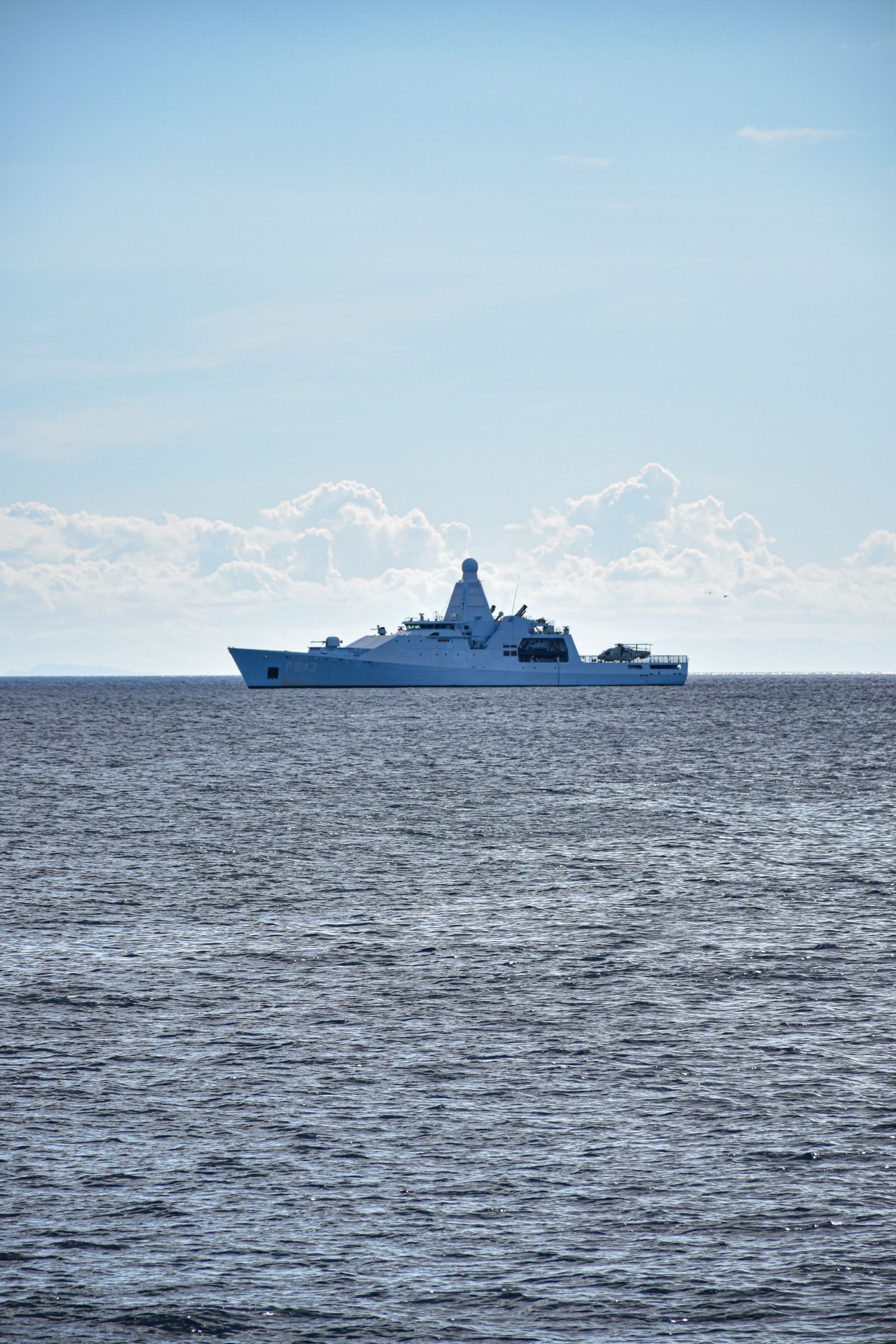 Grey warship underway at sea under a blue sky