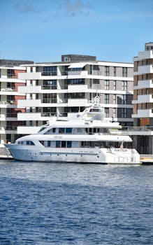 A stunning white yacht named 'FORTITUDE' docked alongside modern waterfront apartments on a sunny day.