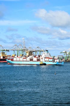 A busy seaport with a cargo ship, cranes, and clear skies.
