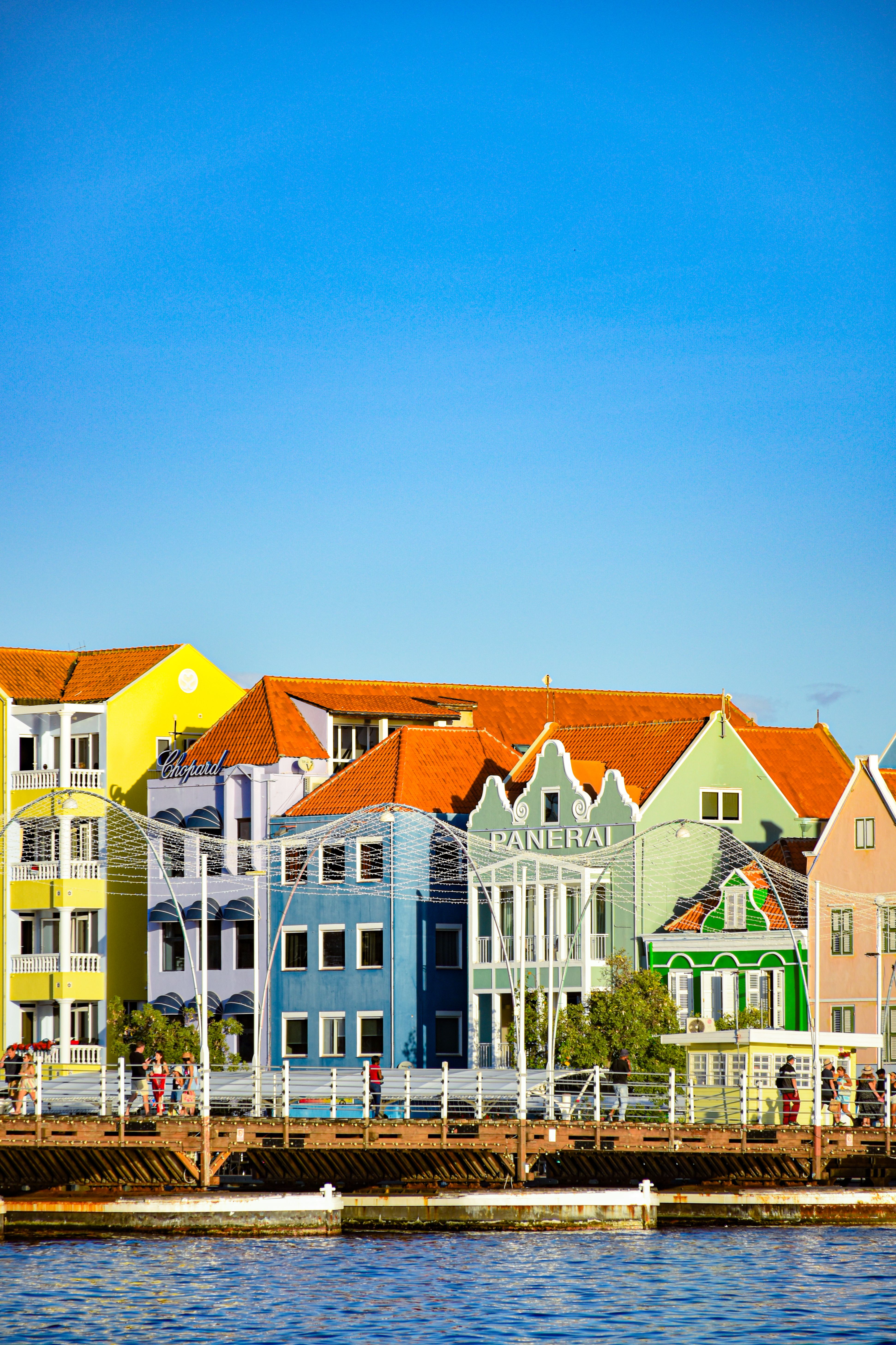 Bezpłatne Tętniące życiem budynki wzdłuż nabrzeża w Willemstad, Curaçao, pod czystym, błękitnym niebem. Zdjęcie z galerii