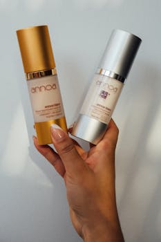 A close-up of a hand holding luxury cosmetic serum bottles with gold and silver caps.