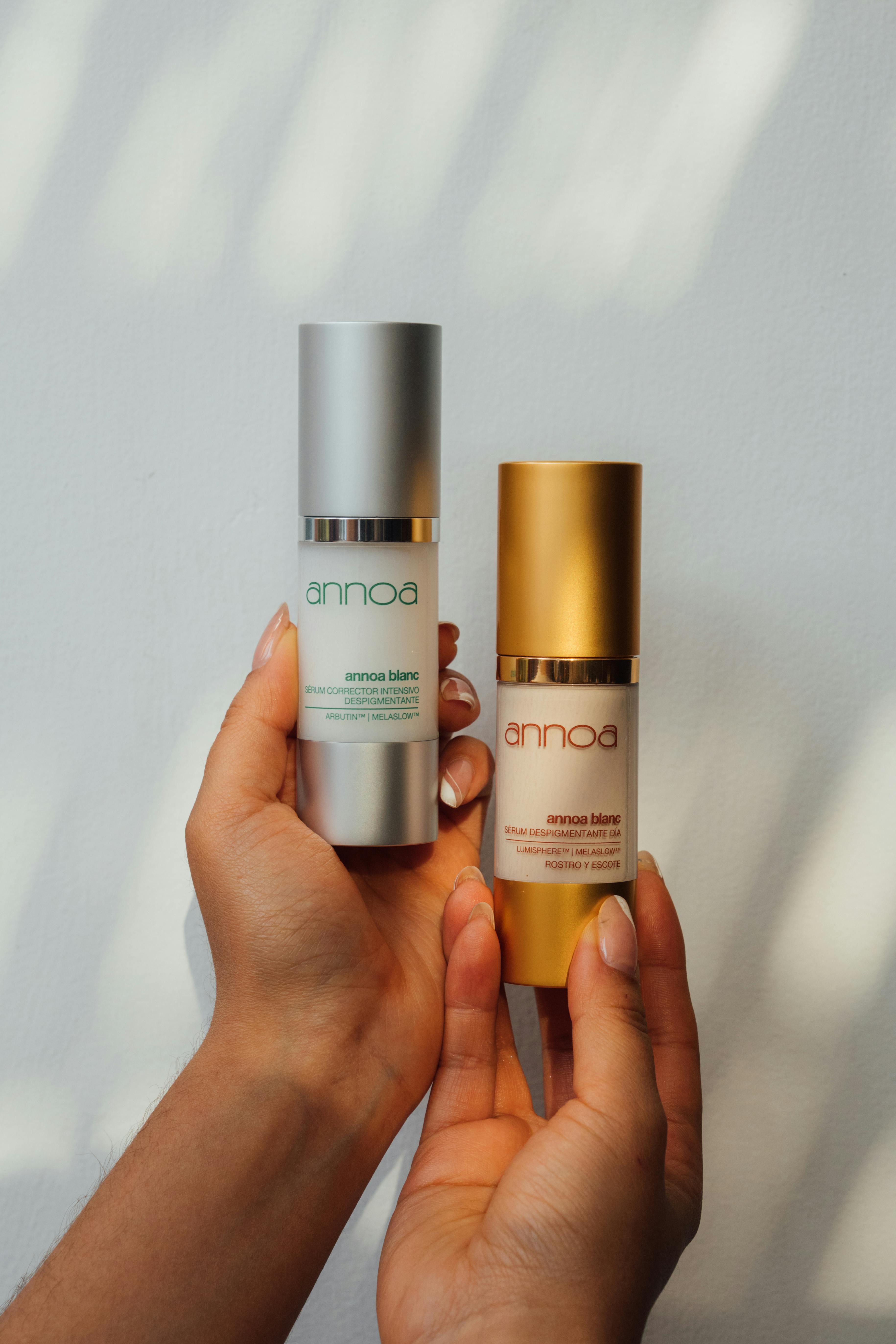 Close-up of hands holding two luxury skincare bottles against a sunlit wall.