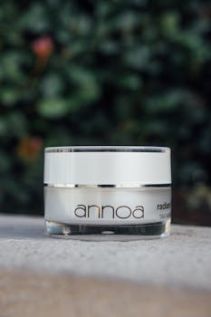 Close-up of luxury skincare cream jar with leafy background, outdoor setting.