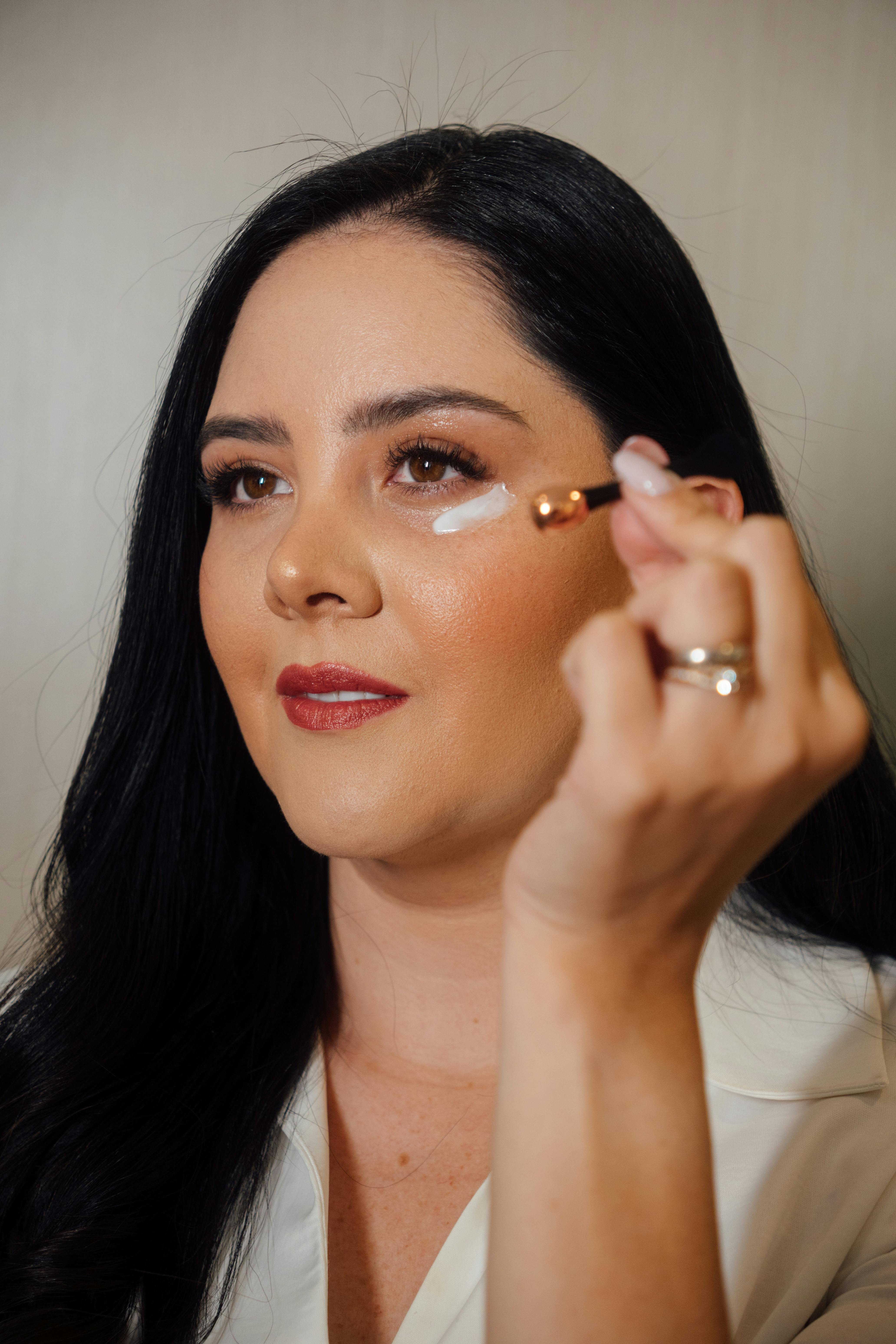 Close-up of woman applying eye cream using a precision brush highlighting skincare routine.