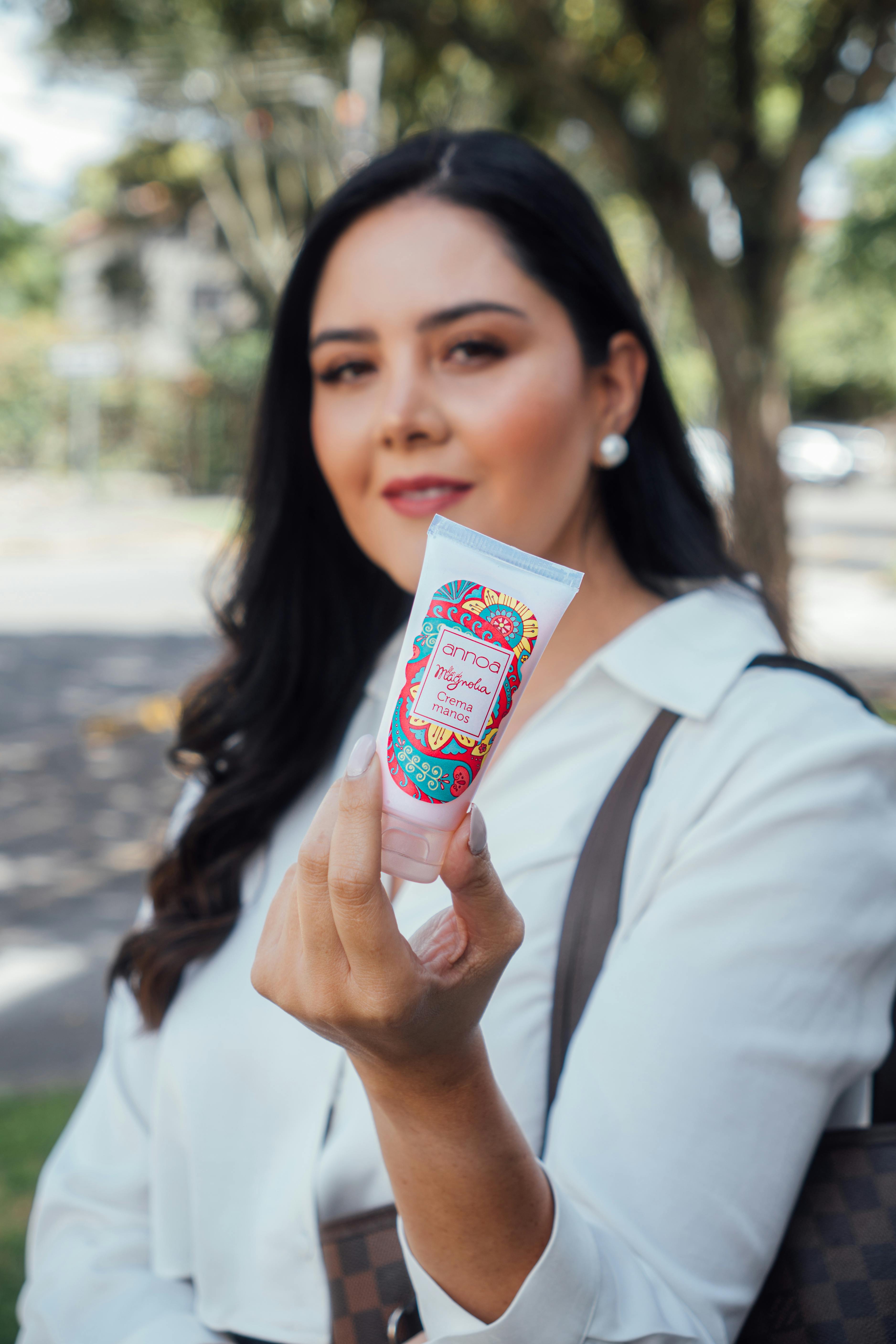 Elegant woman showcasing a skincare product in an outdoor urban setting.