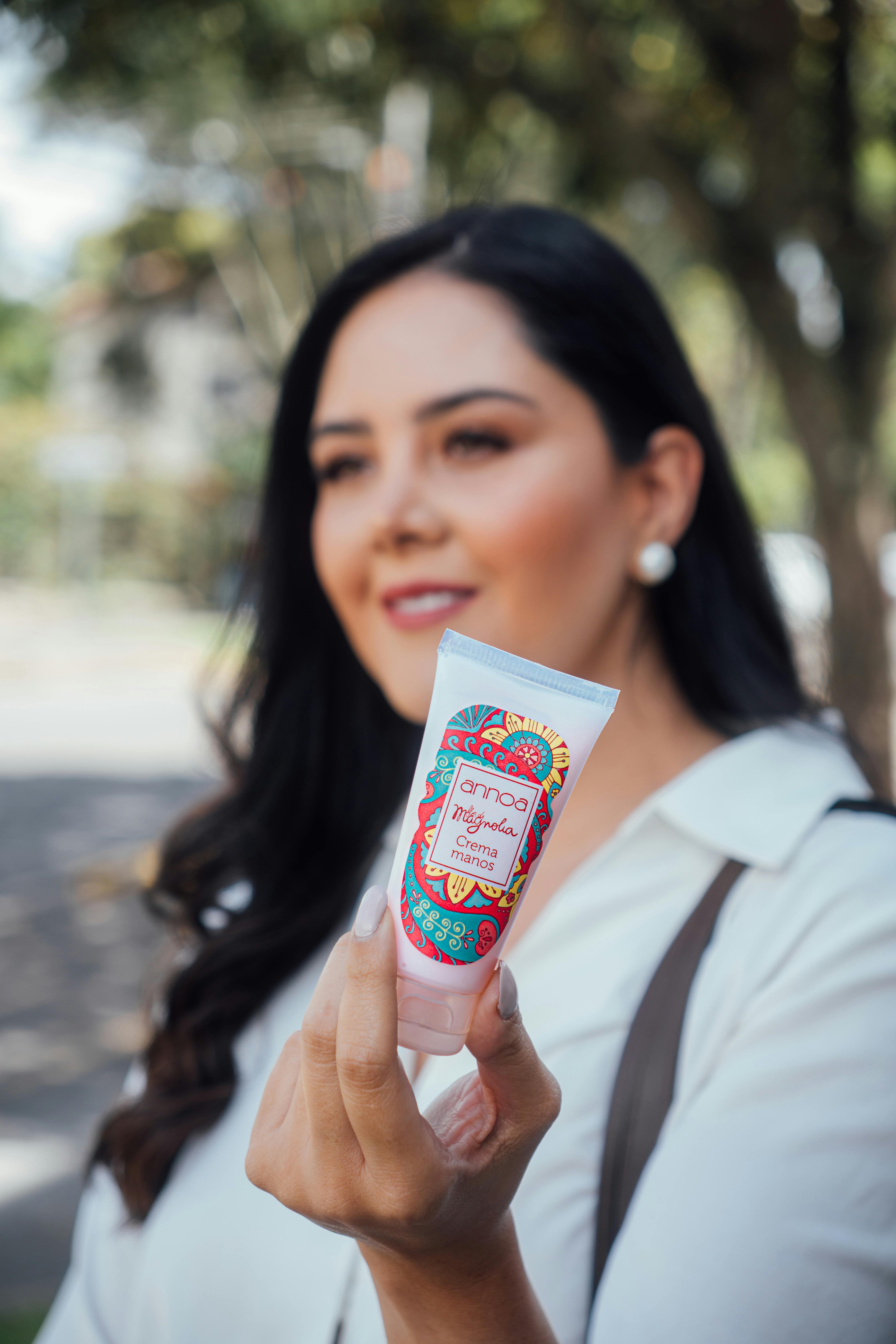 A woman showcasing a beauty cream outdoors, with focus on product label.
