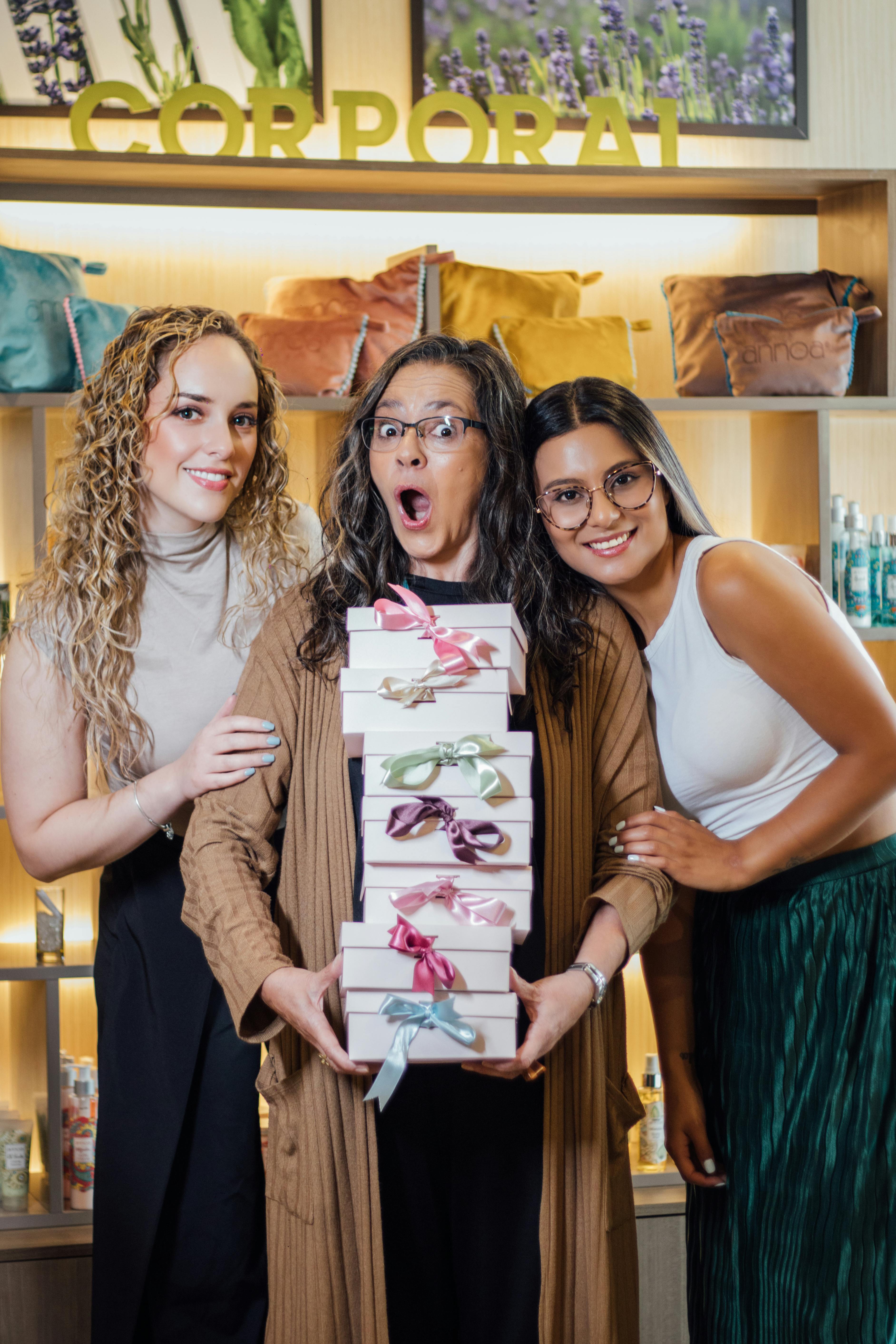 Three women holding gift boxes in a store with skincare products on display.