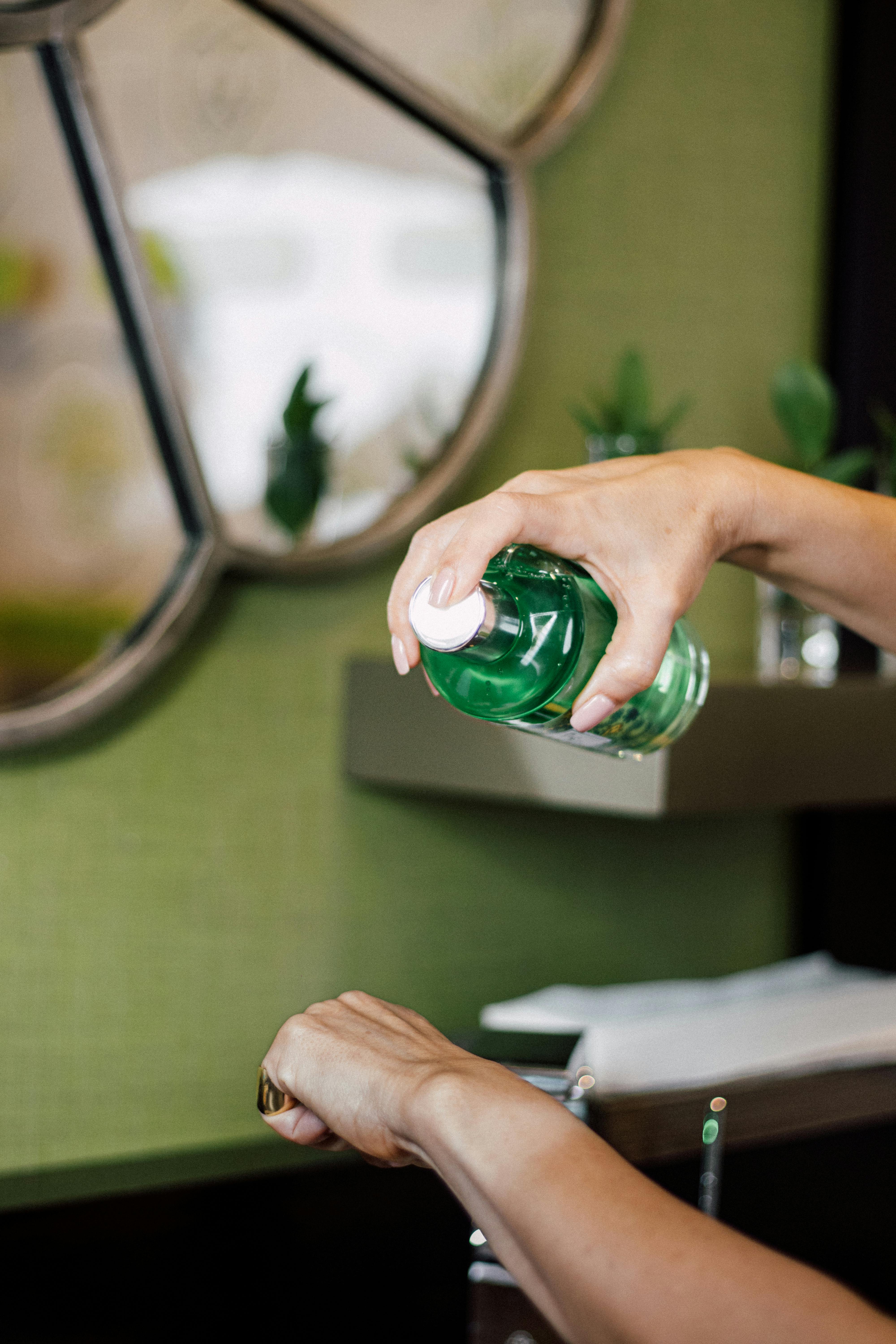 Close-up of hand applying green liquid soap, emphasizing cleanliness and personal hygiene in a stylish bathroom setting.