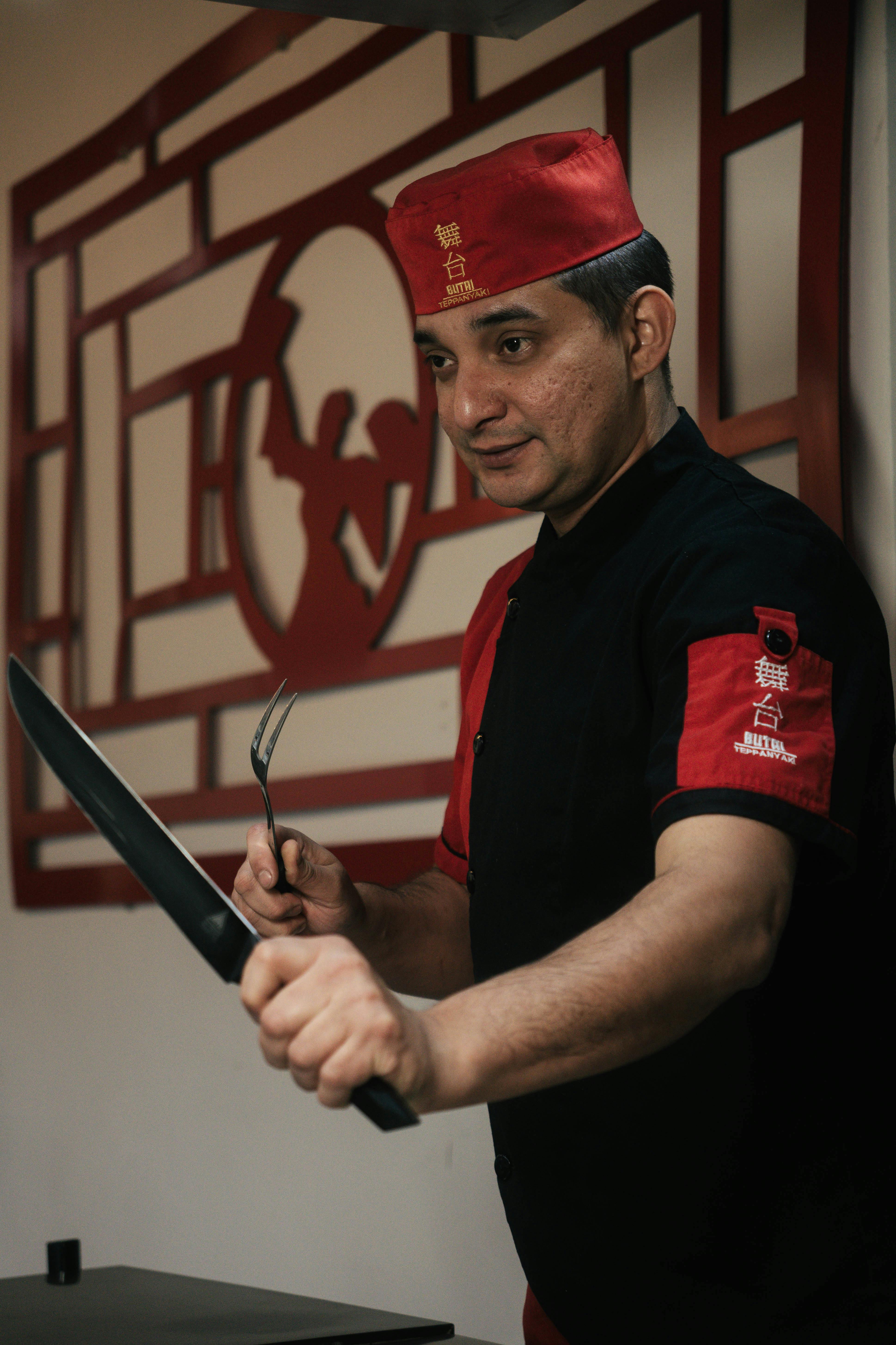 A chef with a knife and fork focused on preparation in a Japanese restaurant setting.