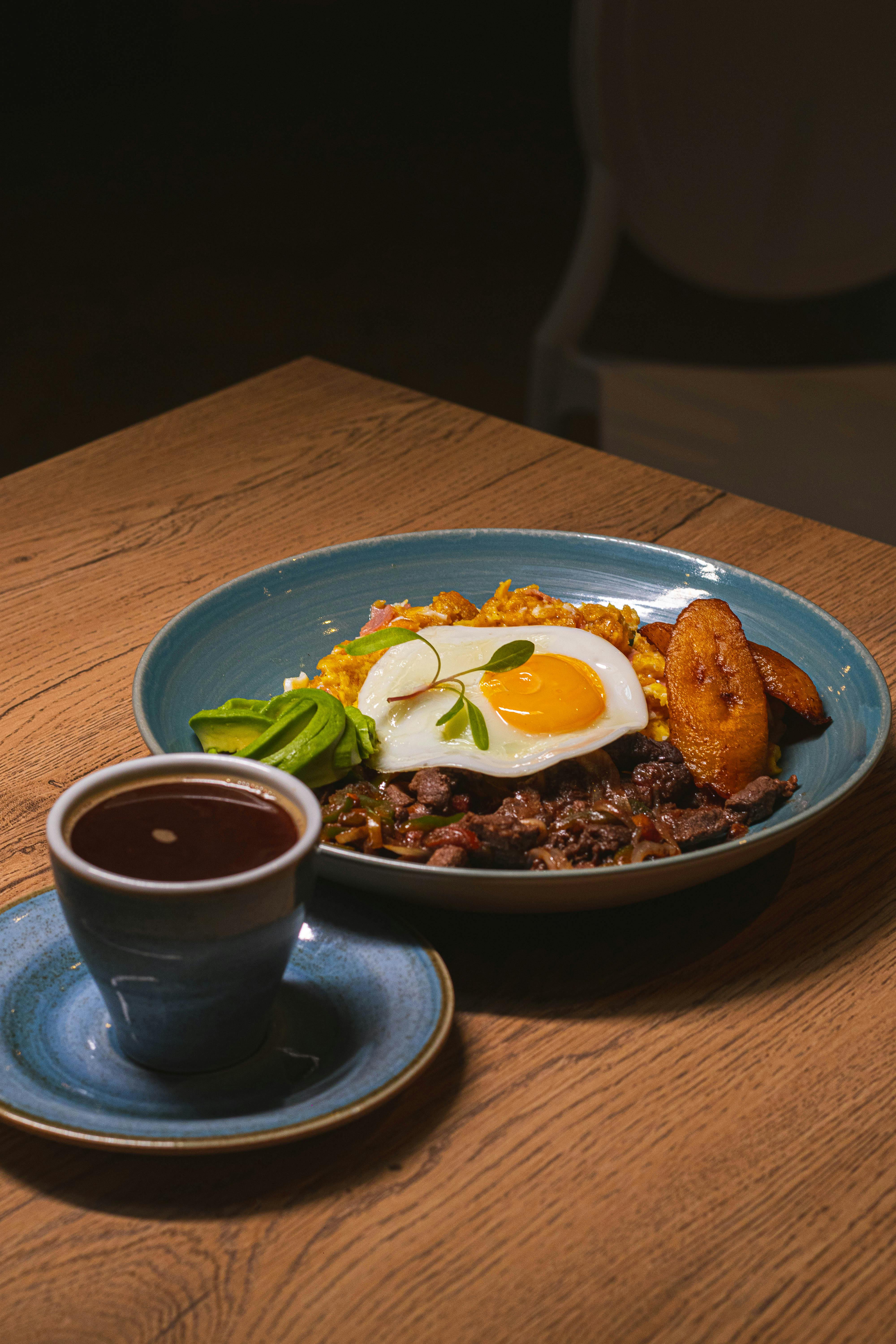 Plate of breakfast with egg, plantain, and coffee on wooden table.