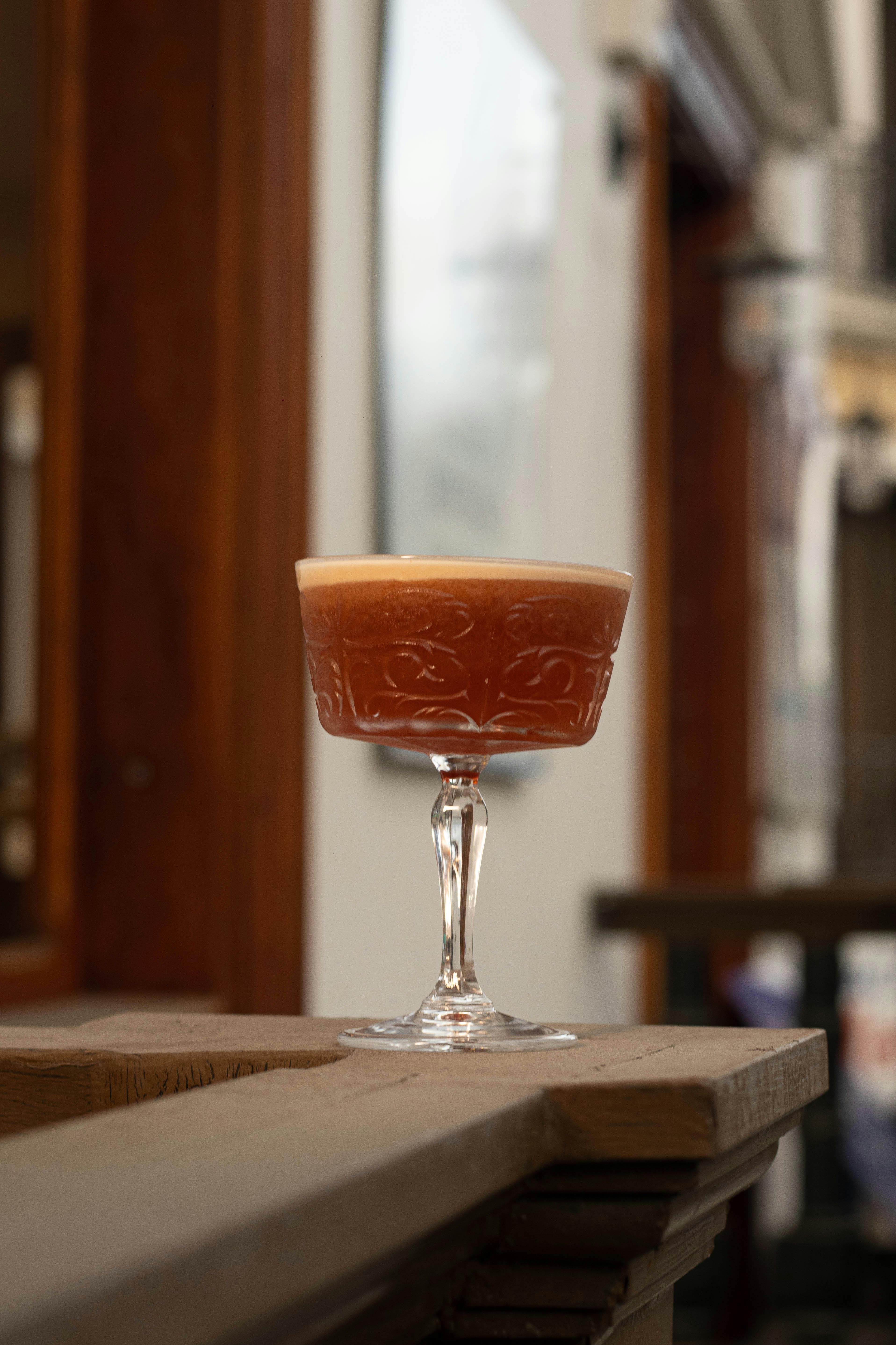 Artistic photo of a cocktail in a decorative glass on a wooden ledge indoors.