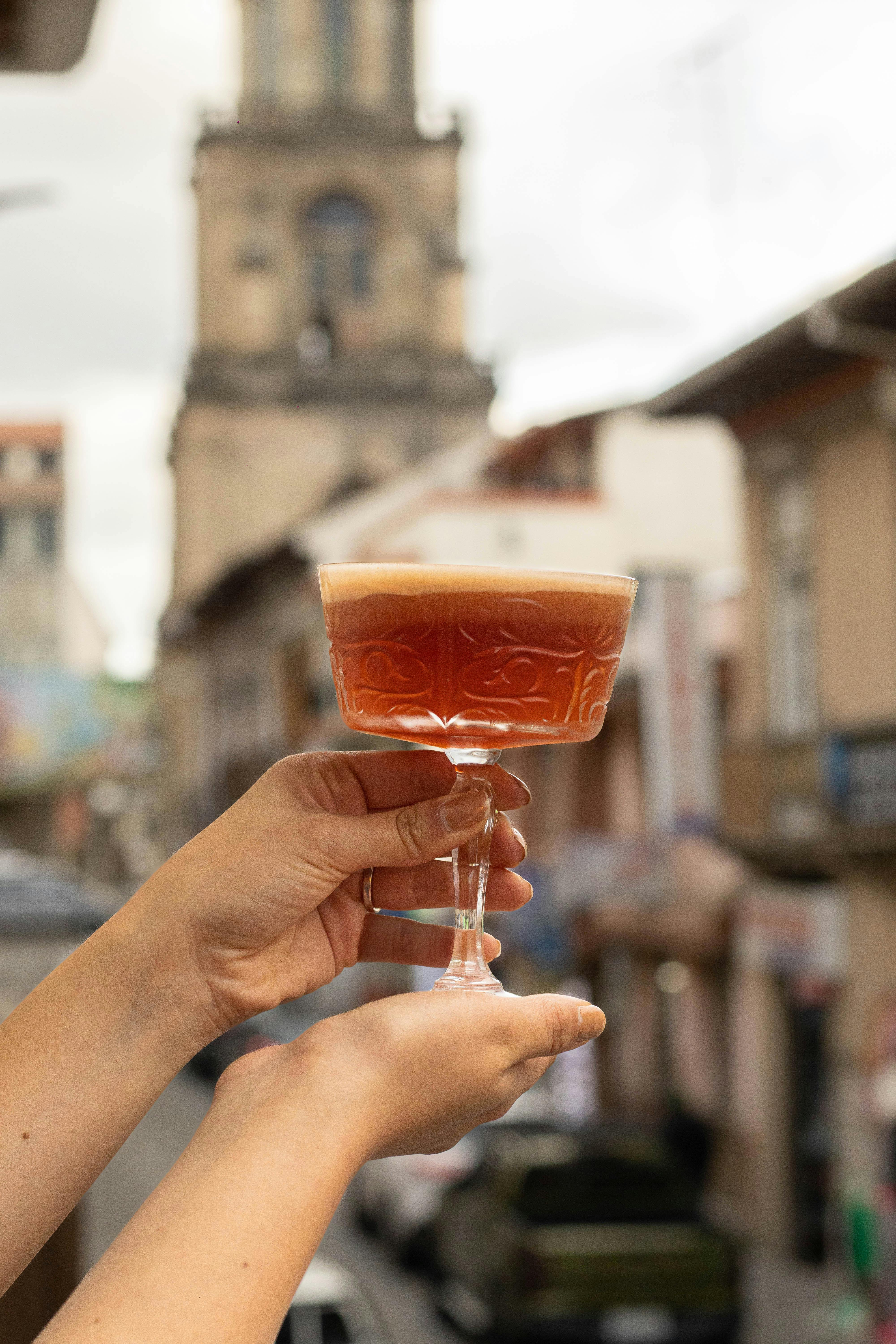 A decorative cocktail glass held against a blurred historic city backdrop, blending modern lifestyle with vintage charm.